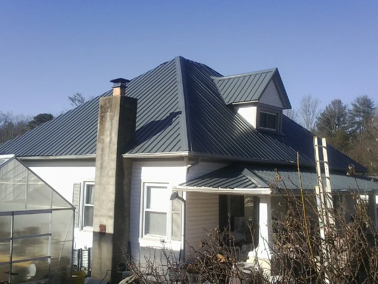 Dark blue standing seam metal roof on a white farmhouse with dormer — Slate & Tile Roof Repair by Roofing Brothers in Boxholm