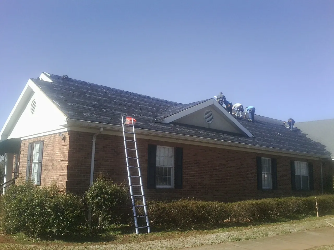 Crew tearing shingles off a brick ranch roof with a ladder set — Emergency Roof Repair work by our crew in Boxholm