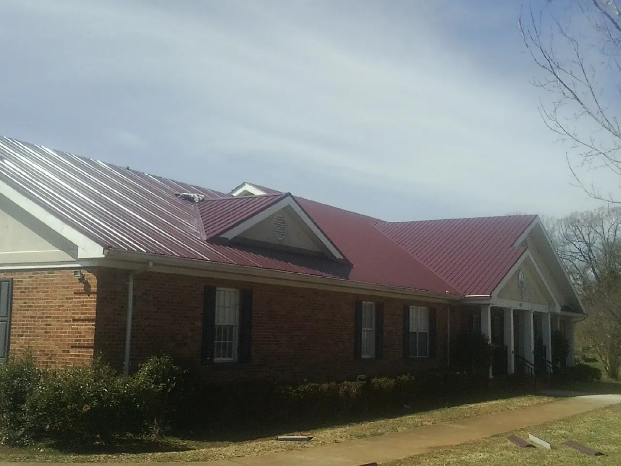 Red metal roof with gabled entries on a long brick building, from a Hail Damage Roof Repair job in Boxholm
