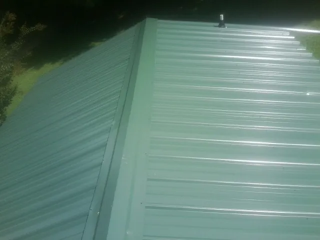 New green metal panels meeting at the ridge of a roof — Flat Roof Repair work by our crew in Boxholm