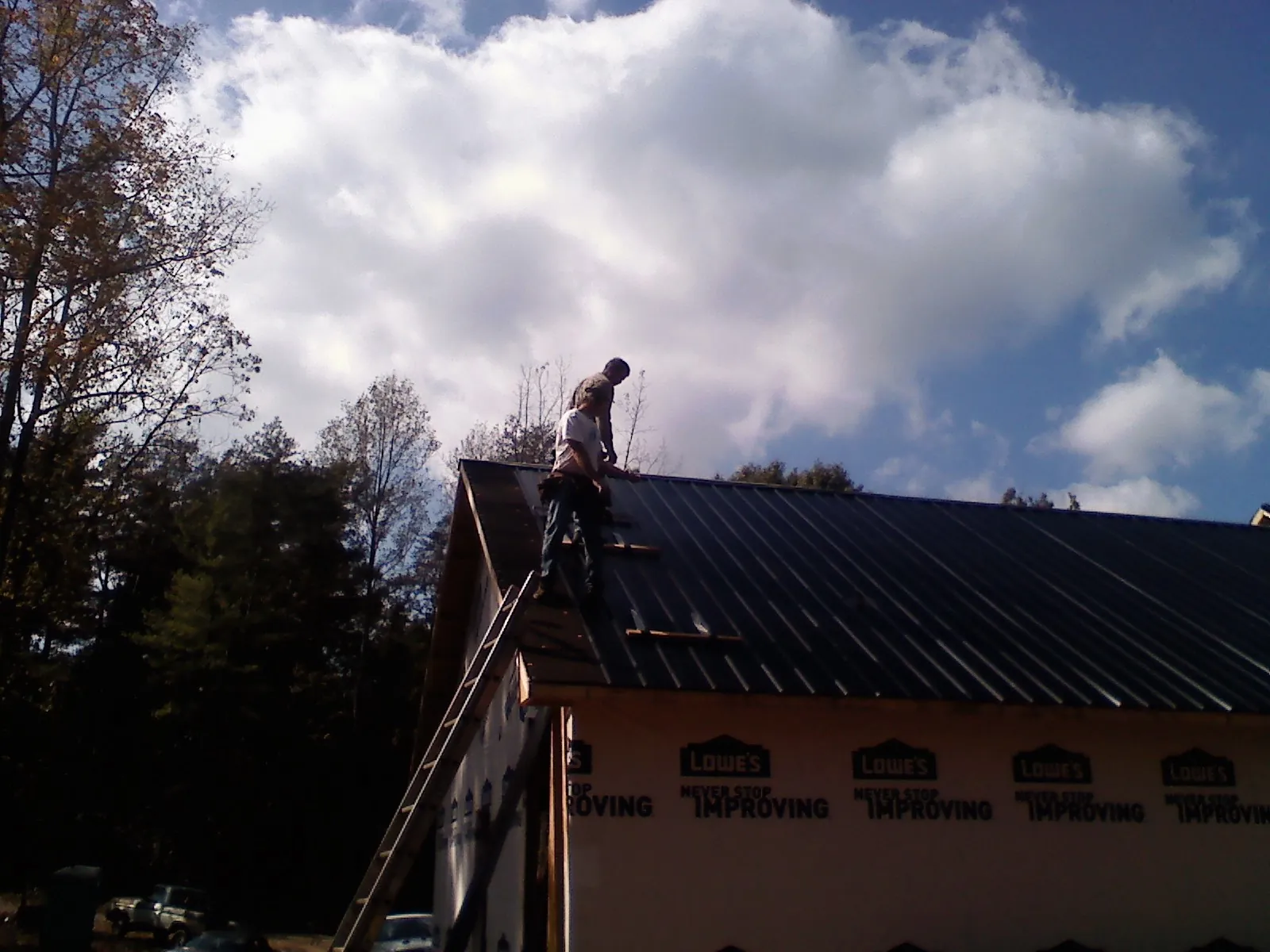 Roofer fastening dark metal panels high against a cloudy sky, from a Roof Inspection job in Boxholm