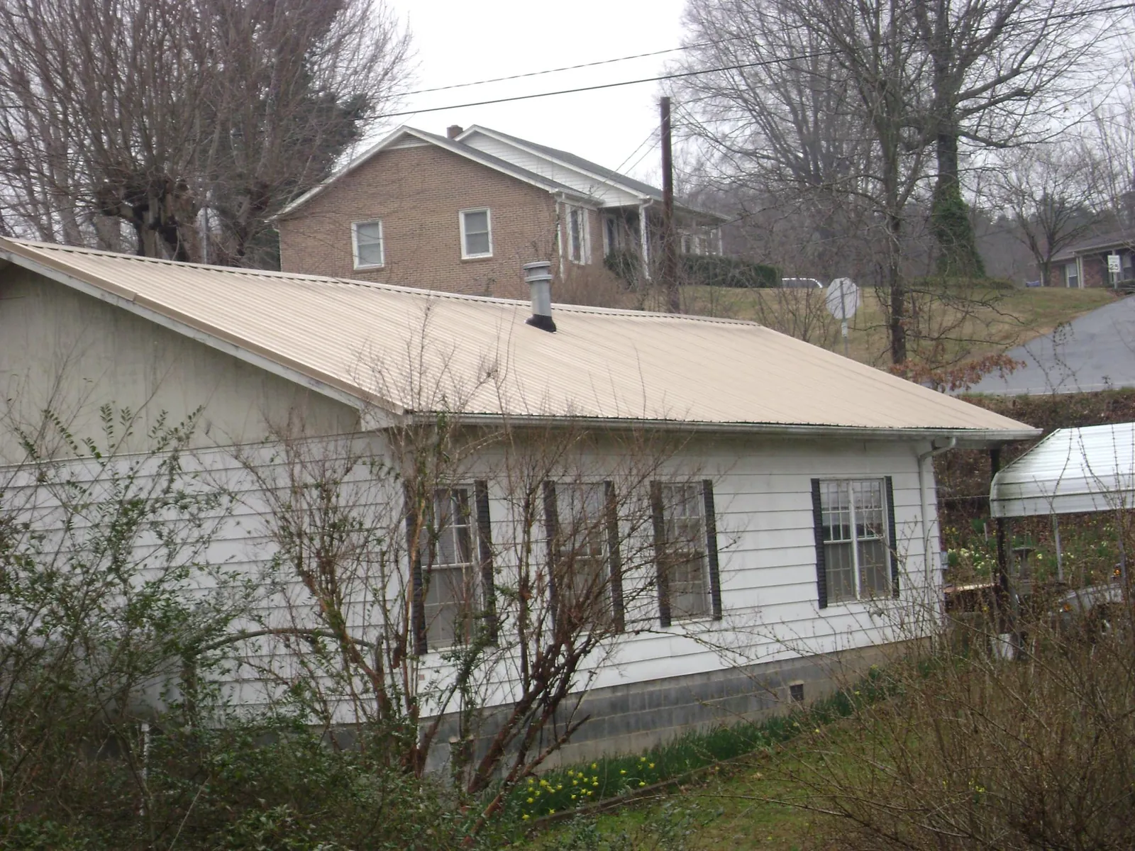 Tan metal roof on a white sided house set into a hillside — Commercial Roofing by Roofing Brothers in Boxholm