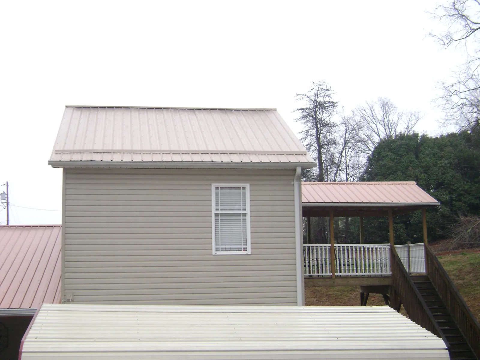Tan metal roofs on a two story addition and attached porch, from a Roof Replacement job in Boxholm